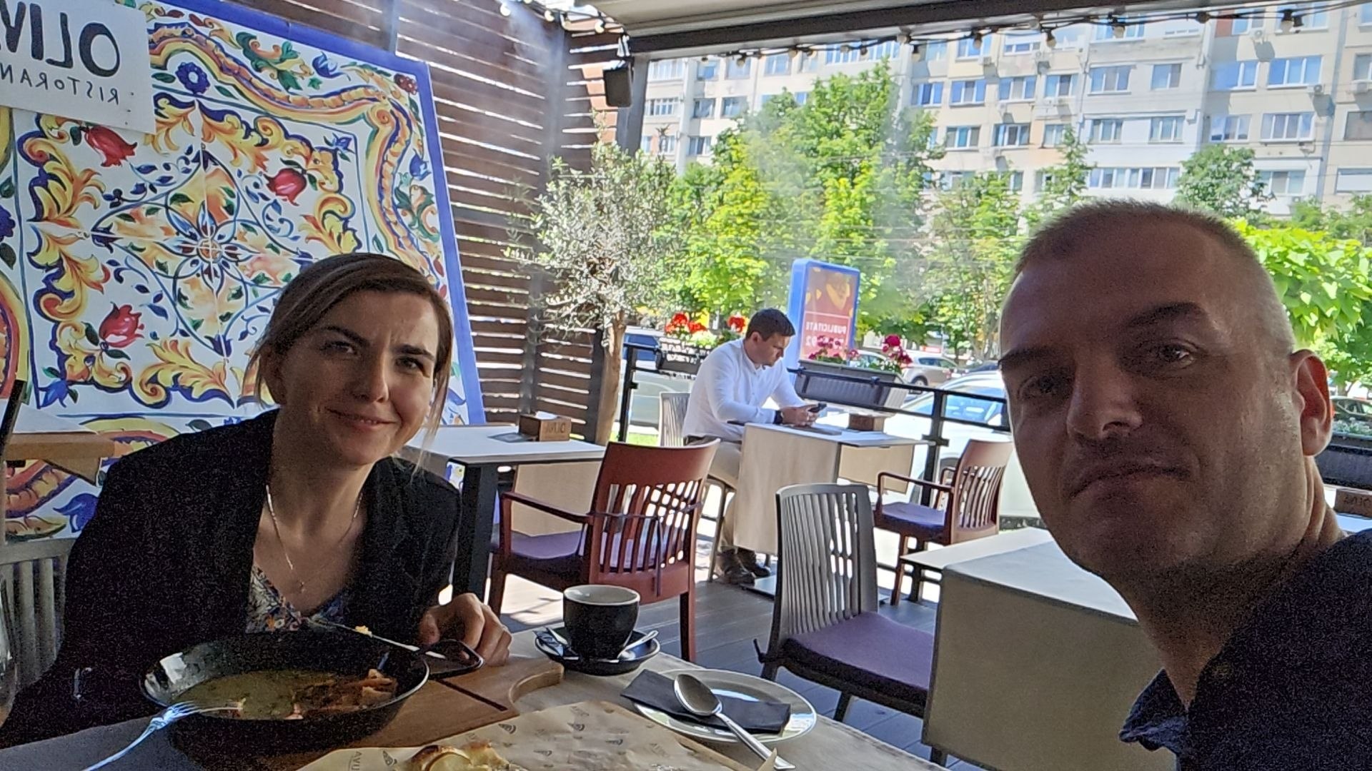 Cristina and a friend enjoying coffee and pizza at a sunny café table.